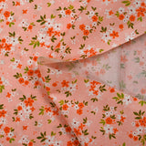 Popeline de coton imprimée composition florale fond rose pêche
