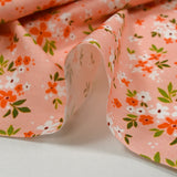 Popeline de coton imprimée composition florale fond rose pêche